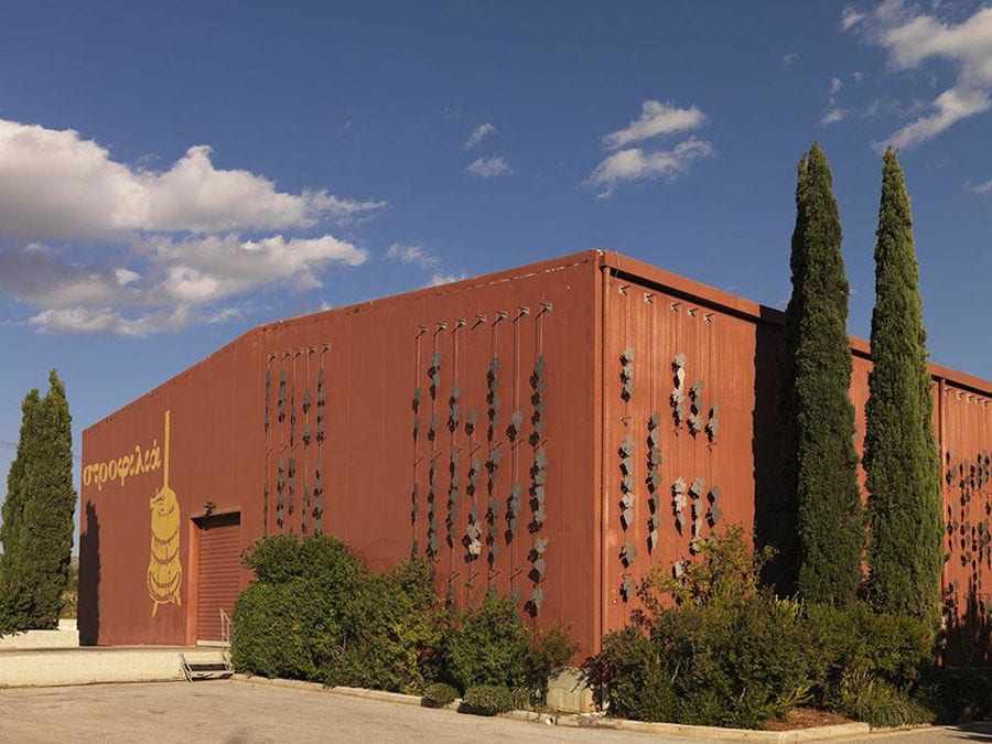 one side of Strofilia winery building with trees and stone pavement in front